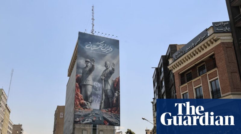 Tall urban mural on a building featuring two men raising their hands, with a dramatic rocky landscape at the base.