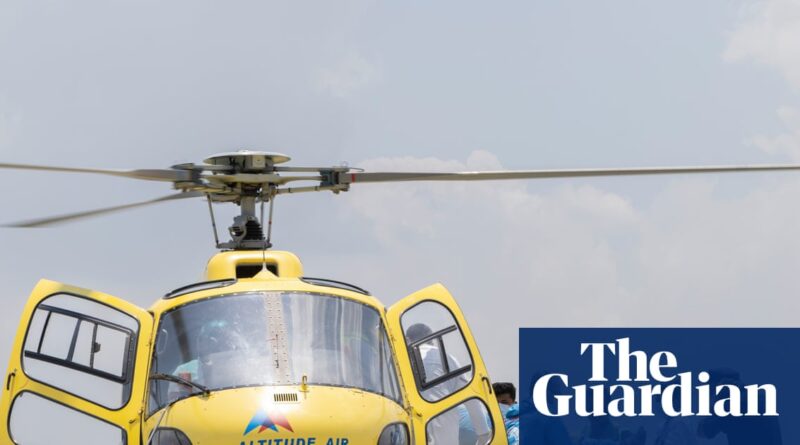 Yellow helicopter with open side doors on a clear day; Guardian logo watermark in the bottom-right corner.