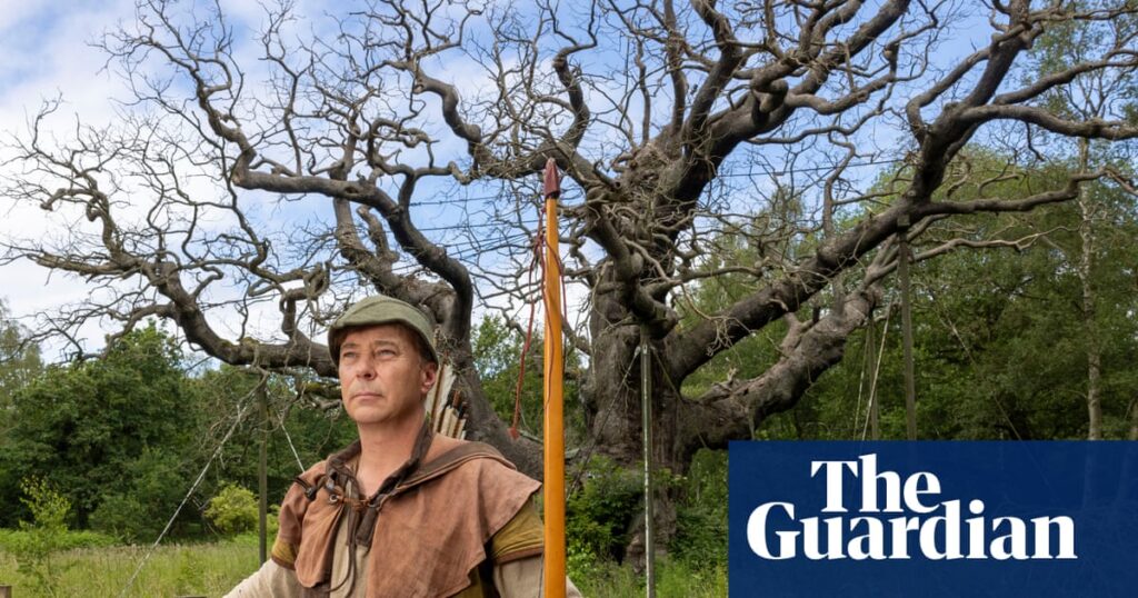 Man in medieval archer attire with a bow and arrows stands before a large bare-branched tree outdoors; Guardian logo overlayed on the bottom right.