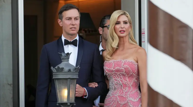 Well-dressed man in a navy tuxedo and bow tie stands with a woman in a pink beaded evening gown as they exit a doorway, holding hands slightly.