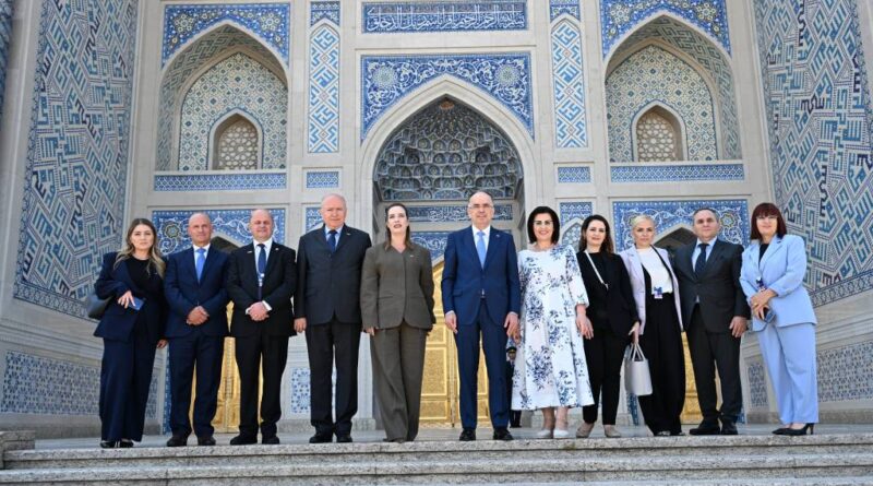 Group of ten professionals in formal attire standing on steps in front of an ornate blue-tiled Islamic facade.