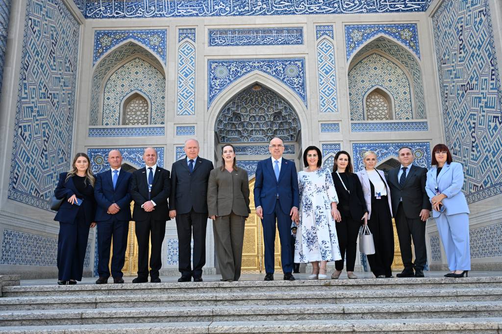 Group of ten professionals in formal attire standing on steps in front of an ornate blue-tiled Islamic facade.