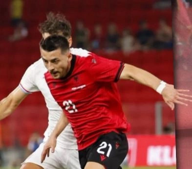 Soccer player in a red jersey number 21 dribbles the ball past a defender on a stadium pitch with red seats in the background.