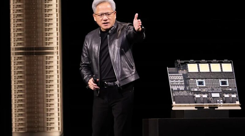Male presenter in a black leather jacket gestures to the audience on a dark stage, with a large server motherboard displayed on a stand beside him.