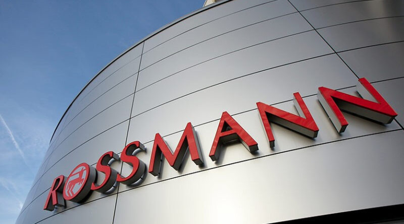 Rosmann store sign on a curved silver facade with red letters against a blue sky.