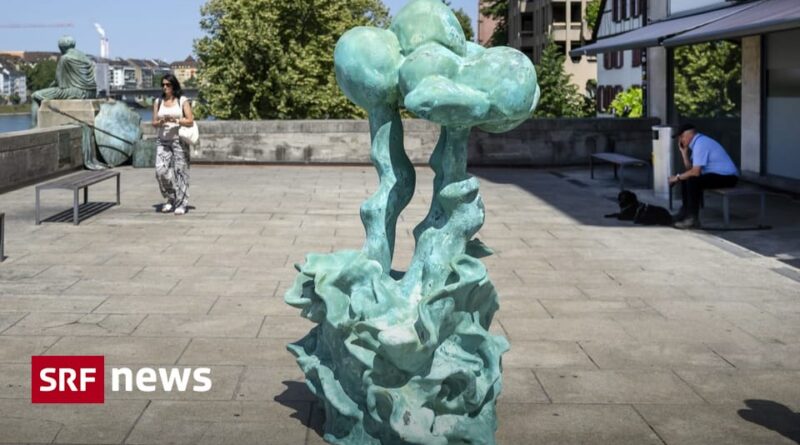 Green abstract sculpture in a sunny public square with pedestrians and a man sitting nearby; SRF News watermark in the corner.