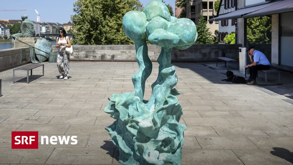 Green abstract sculpture in a sunny public square with pedestrians and a man sitting nearby; SRF News watermark in the corner.
