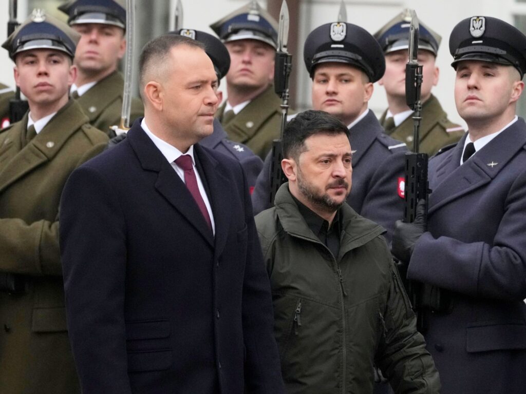 Two civilians stand in front of a line of soldiers in uniform, some holding rifles, at a formal ceremony.