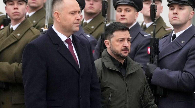 Two civilians stand in front of a line of soldiers in uniform, some holding rifles, at a formal ceremony.