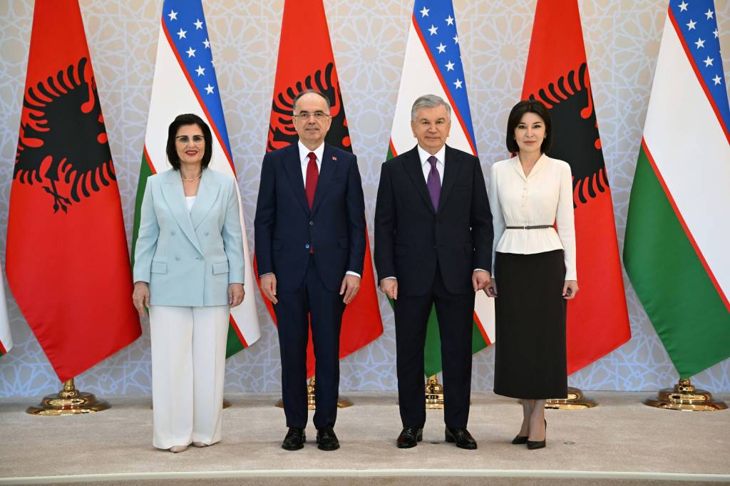 Four officials stand in a row in front of alternating Albanian and Uzbek flags during a formal diplomatic photo.** This seems to have a stray asterisks; remove in final.