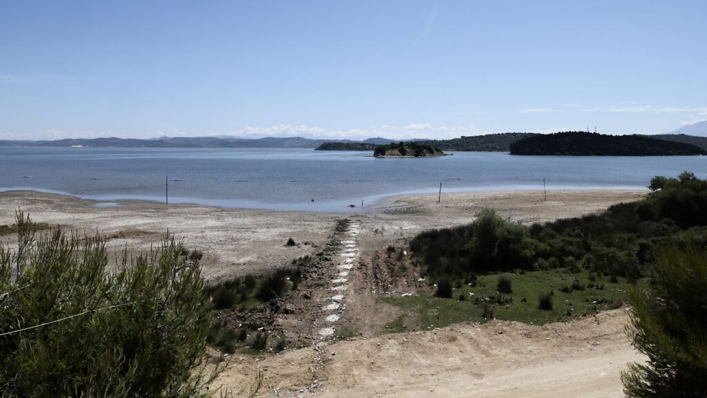 Stone stepping path leading to a calm bay with two small islands and sandy shore under a clear blue sky.