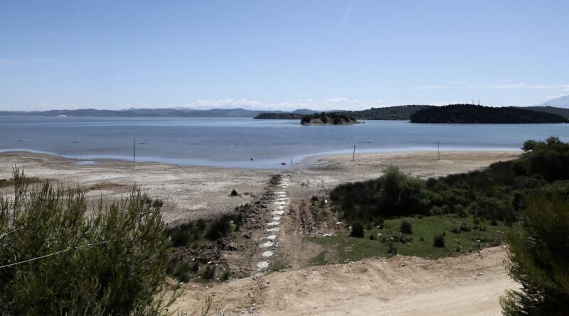 Stone stepping path leading to a calm bay with two small islands and sandy shore under a clear blue sky.