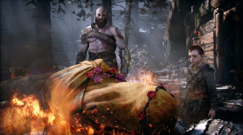 Kratos and a young companion stand beside a flower-adorned corpse on a burning funeral pyre in a snowy forest setting.
