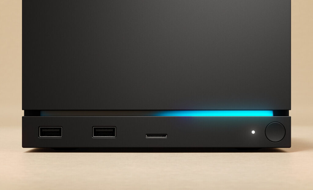 Front view of a black computer tower with two USB-A ports, a slim media/SD card slot, a blue LED glow, and a circular power button with a small indicator light.