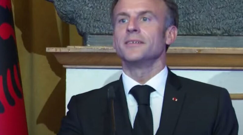 Man in a suit giving a speech at a podium with a blue-red-white banner in front.