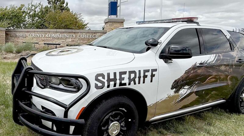 White Sheriff SUV with a heavy front bumper and large 'SHERIFF' decal parked on grass near a county community college sign.