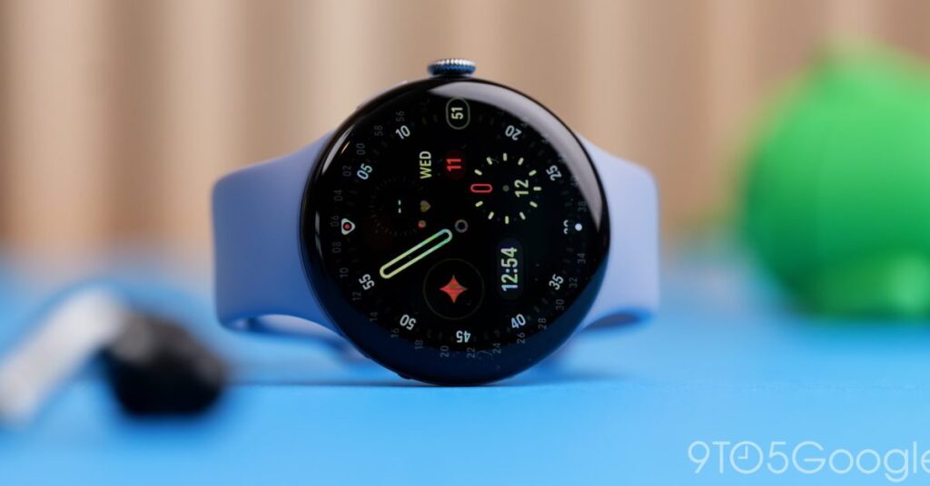 Blue smartwatch with a round black face and light blue band resting on a blue surface, showing the time and date on the display