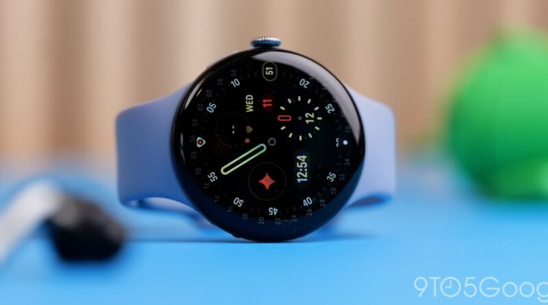 Blue smartwatch with a round black face and light blue band resting on a blue surface, showing the time and date on the display