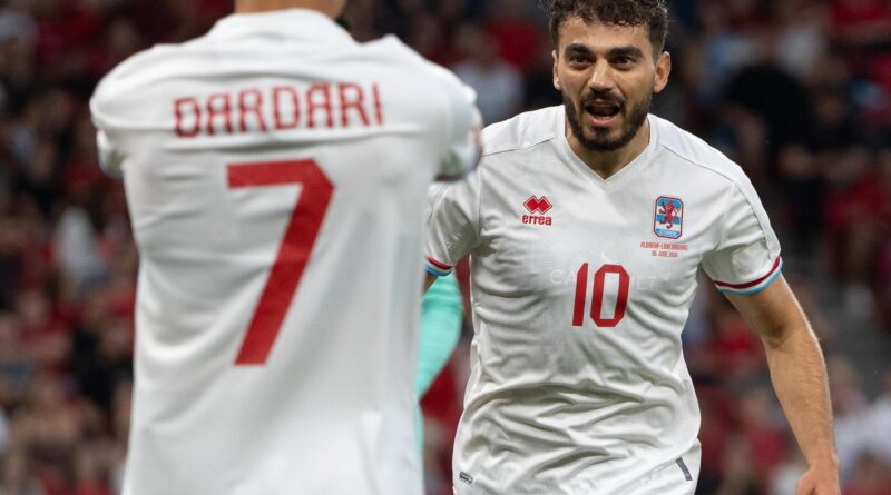 Soccer players in white jerseys celebrating on the pitch; back of a teammate shows 'DARDARI' and number 7 on his shirt (left).