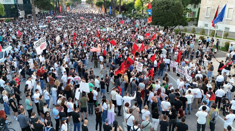 Large crowd of protesters filling a city street, many holding red flags and signs.—overhead view of a demonstration