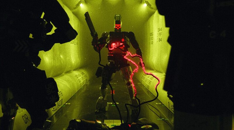 Humanoid combat robot with red glowing chest and energy whip stands in a narrow yellow-lit corridor, flanked by shadowy figures.