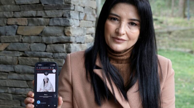 Woman in a tan coat outdoors holds up a smartphone displaying a portrait on its screen (the phone is near her chest).