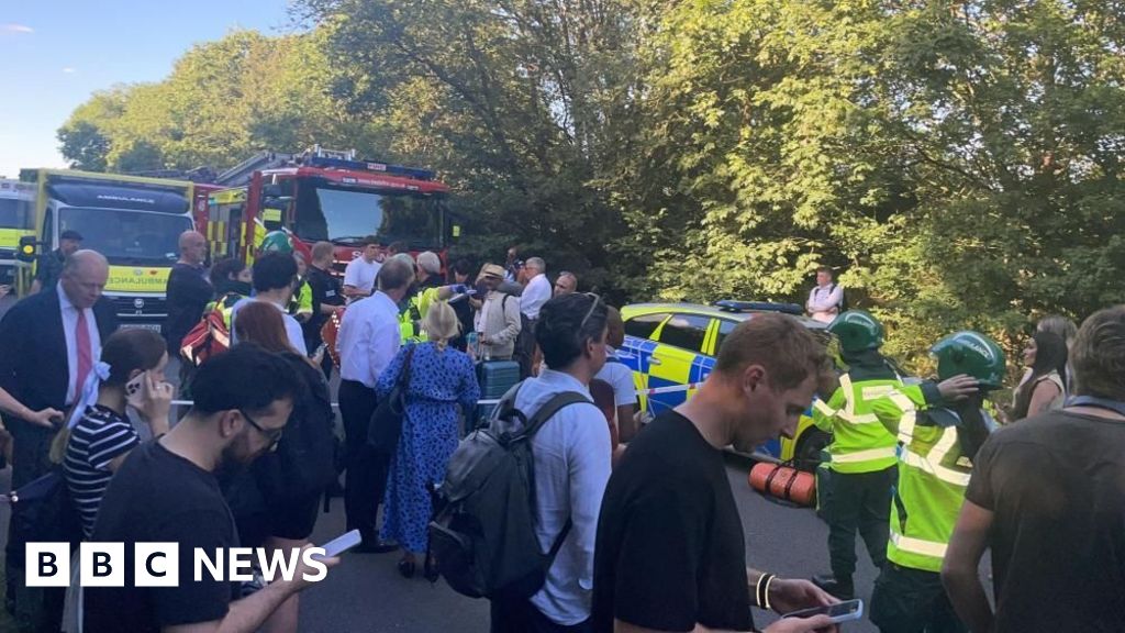 Crowd gathers on a street with emergency vehicles, police cars, and firefighters; BBC News watermark in the corner.