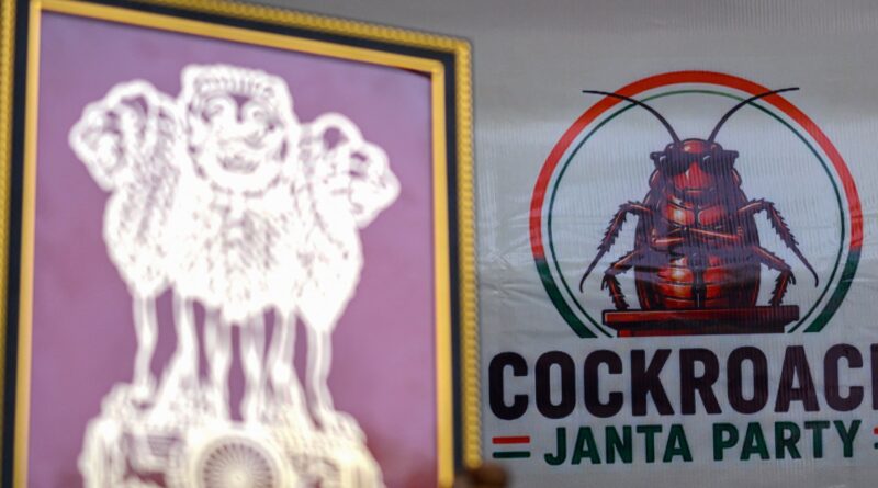 Close-up of a political campaign sign featuring a stylized cockroach inside red/green circles, with the word 'COCKROACH' and 'JANTA PARTY' visible; a purple-framed badge is beside it.