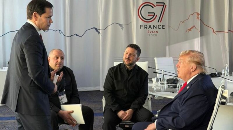Four men in a meeting room: one standing in a suit talks to three seated colleagues, with a France Evian 2026 banner in the background.