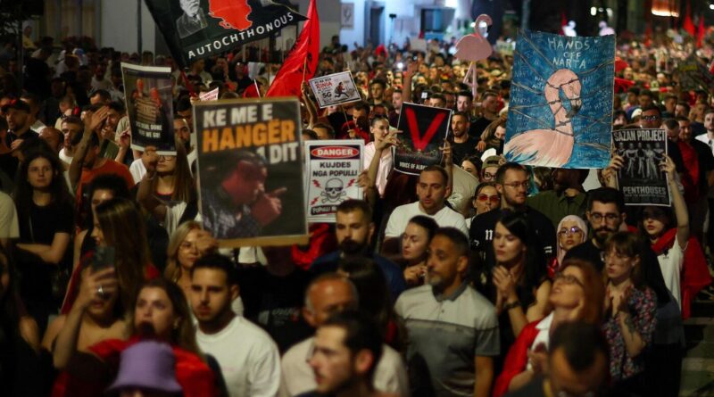 A large, diverse crowd of protesters marching at night, holding various handmade signs and banners.