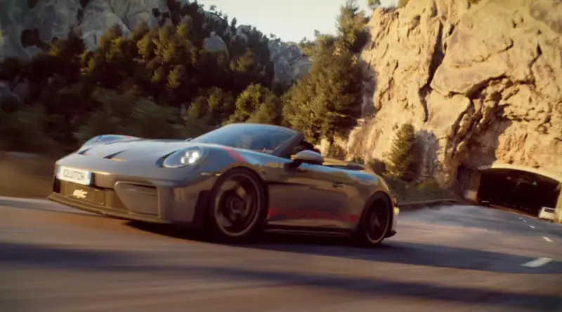 A gray sports car speeding along a winding mountain road with rocky cliffs and a tunnel in the distance.