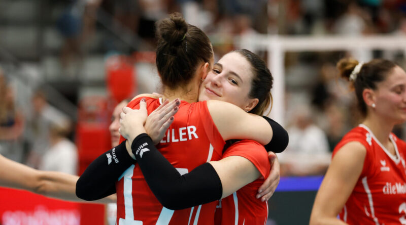 Two volleyball players in red uniforms hug on the court, celebrating a point.
