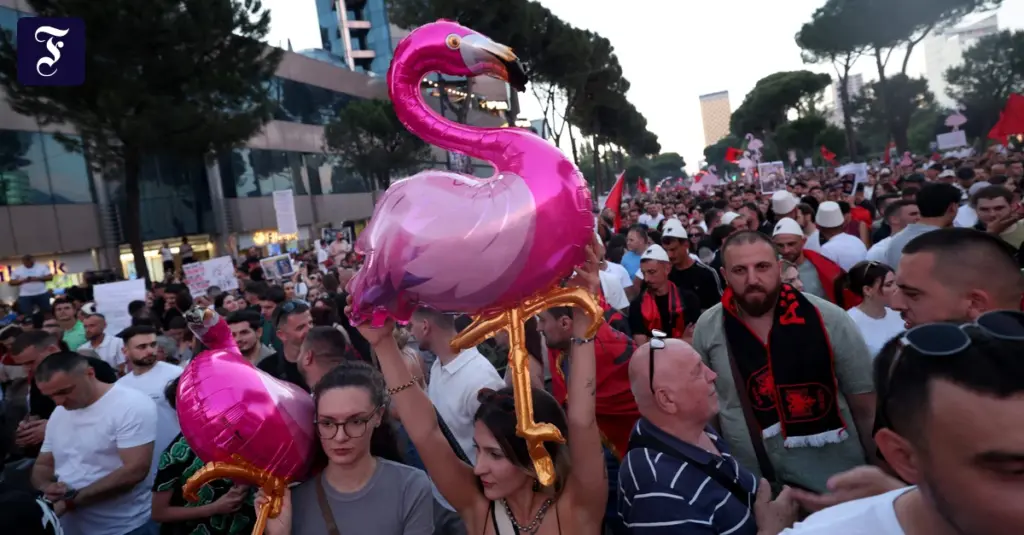 Large crowd of protesters in a city street, many holding signs, with prominent pink flamingo balloons in the foreground behind them.