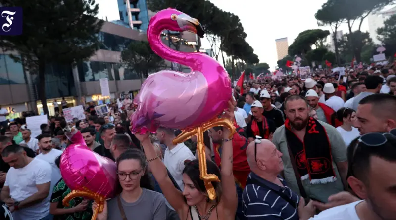 Large crowd of protesters in a city street, many holding signs, with prominent pink flamingo balloons in the foreground behind them.