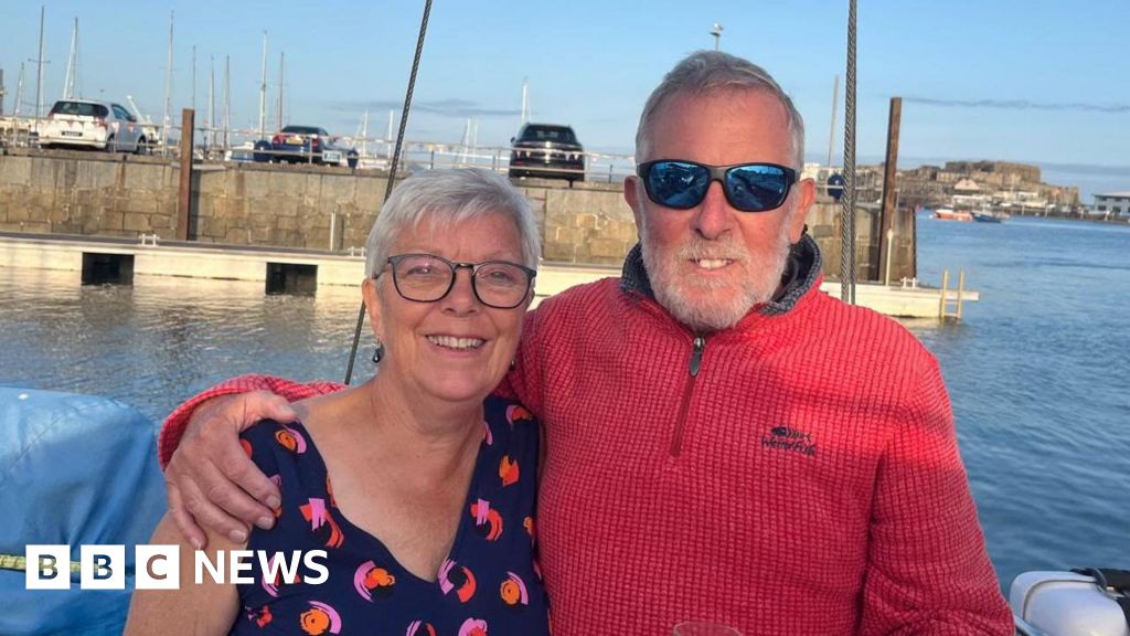 Smiling elderly couple with arms around each other at a marina, boats and water in the background; BBC News watermark visible.