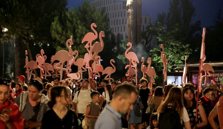 Crowd of people at a nighttime outdoor festival with tall pink flamingo sculptures rising above the attendees.