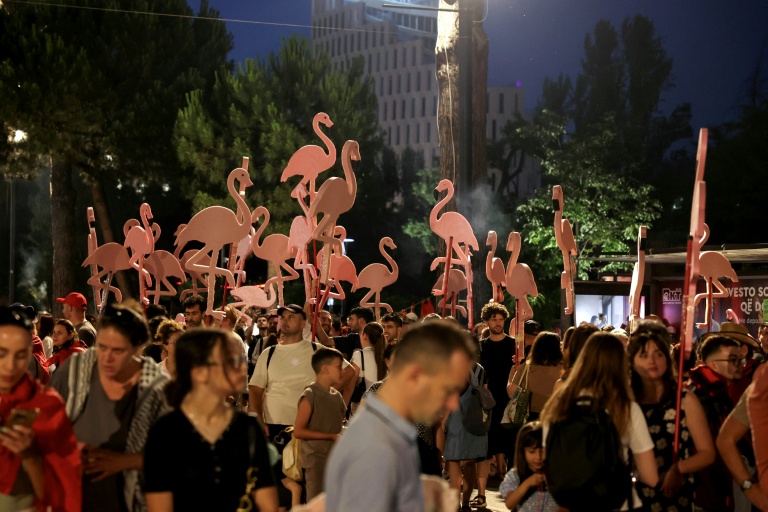 Crowd of people at a nighttime outdoor festival with tall pink flamingo sculptures rising above the attendees.