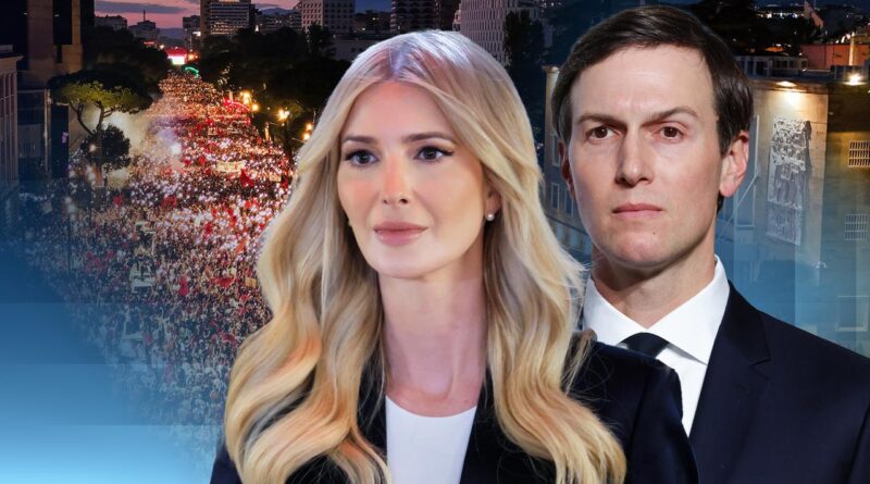 Two well-dressed adults, a man and a woman, stand in the foreground with a large urban crowd at a nighttime rally behind them.