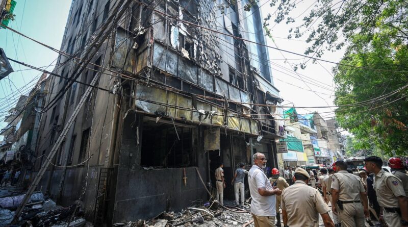Burnt, multi-story building with charred exterior and tangled wires; crowd and beige-uniform police/officers on the street.