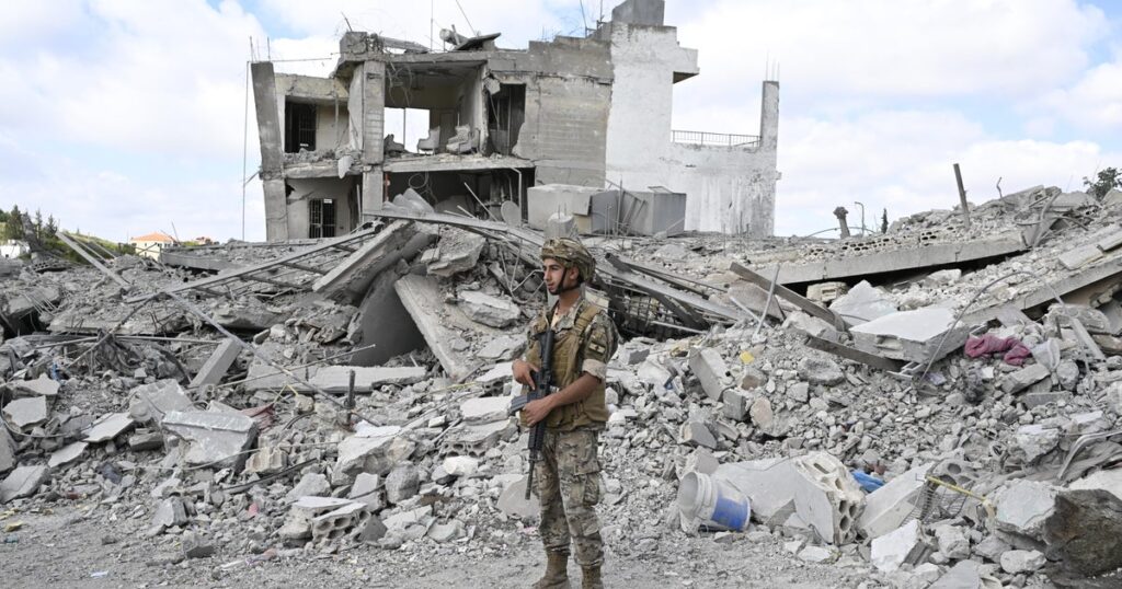 Soldier in camouflage and helmet stands amid rubble of a destroyed building with scattered concrete and debris.