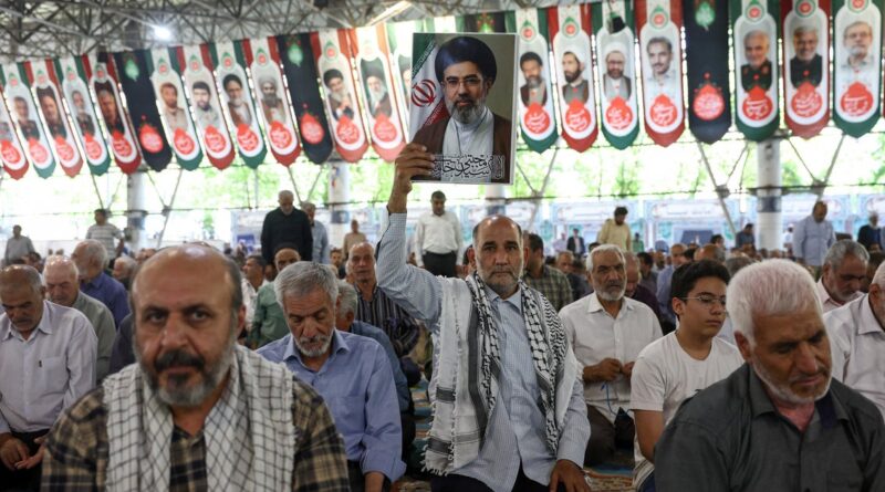 Man in a crowded hall raises a framed portrait of a religious leader during a bannered event.
