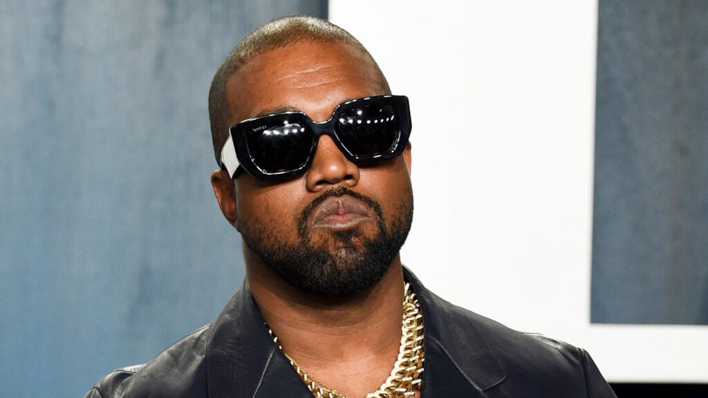 Close-up of a man with a shaved head wearing oversized black sunglasses and a gold chain.