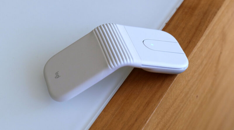 White Logitech wireless presenter remote with a ridged grip and a small blue status LED resting on a wooden desk next to a laptop.
