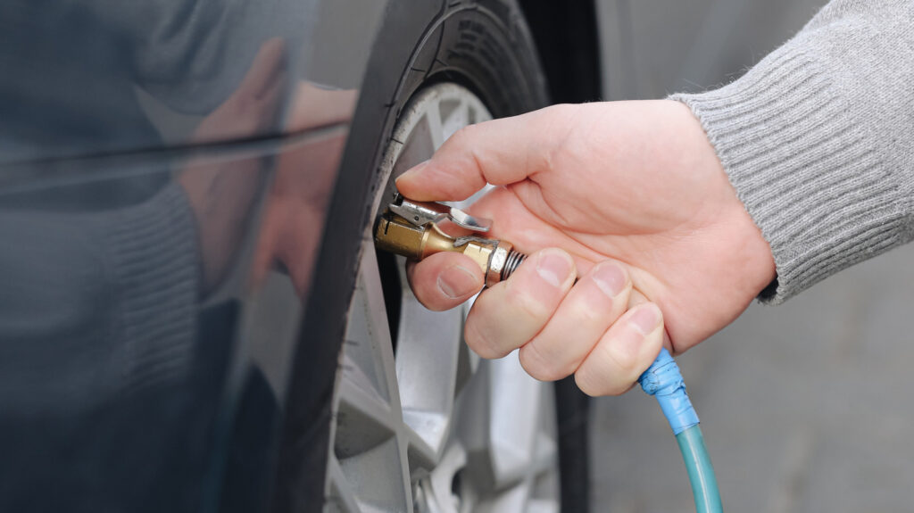 Close-up of a hand connecting an air hose to a car tire valve to inflate it.