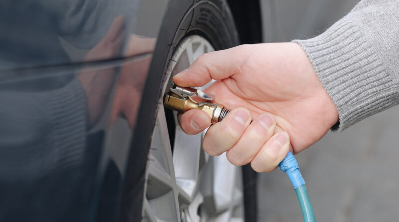 Close-up of a hand connecting an air hose to a car tire valve to inflate it.