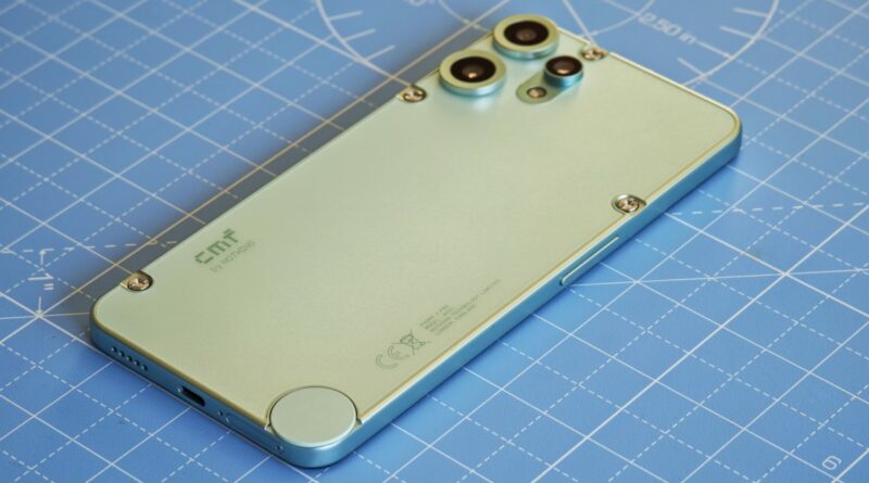 Back of a green smartphone with triple camera module in top-left corner on a blue grid cutting mat, with small screws visible and a circular sensor at the bottom edge.