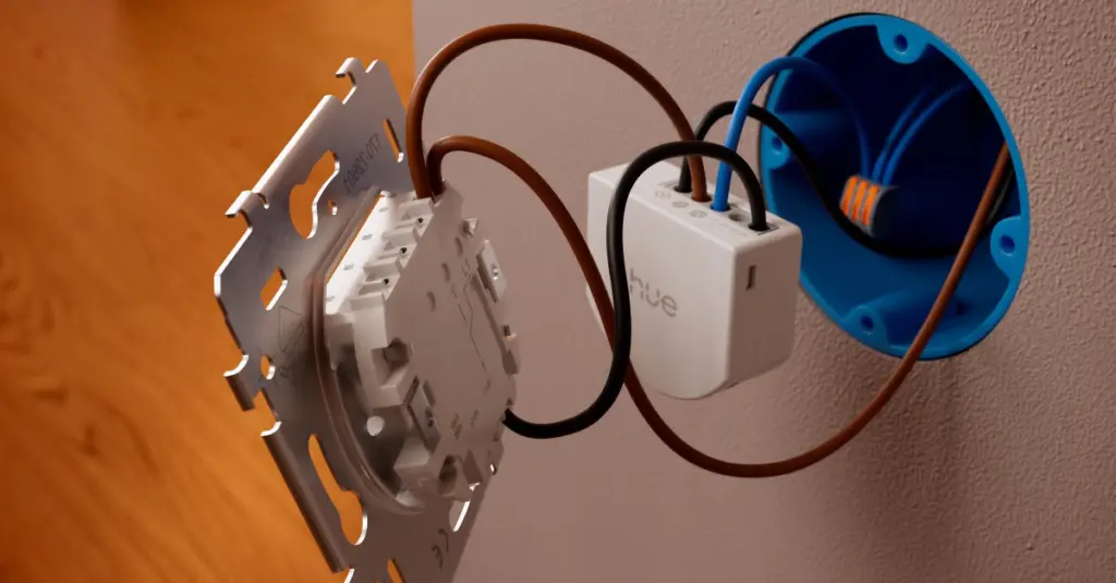 Exposed wall wiring with a white Hue smart switch module connected to brown and blue conductors. (installation in progress)