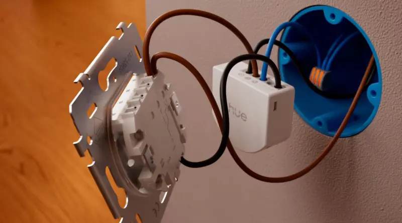 Exposed wall wiring with a white Hue smart switch module connected to brown and blue conductors. (installation in progress)