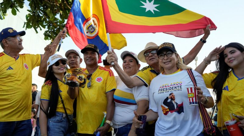 Crowd of supporters in yellow shirts waving flags and cheering at an outdoor rally.