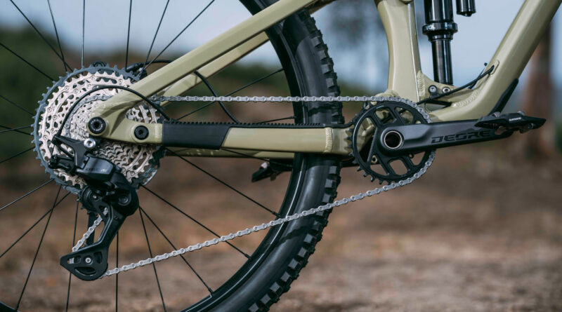 Close-up of a mountain bike rear drivetrain: cassette, chain, derailleur, and beige frame.